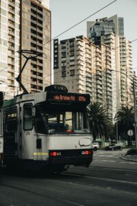 Tram moving through city street with skyscrapers in Melbourne, showcasing urban public transport.